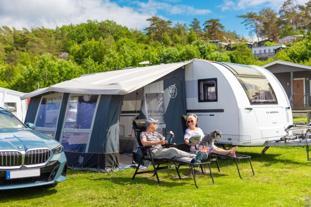 Par kopplar av i campingstolar tillsammans med sin hund utanför en husbil.