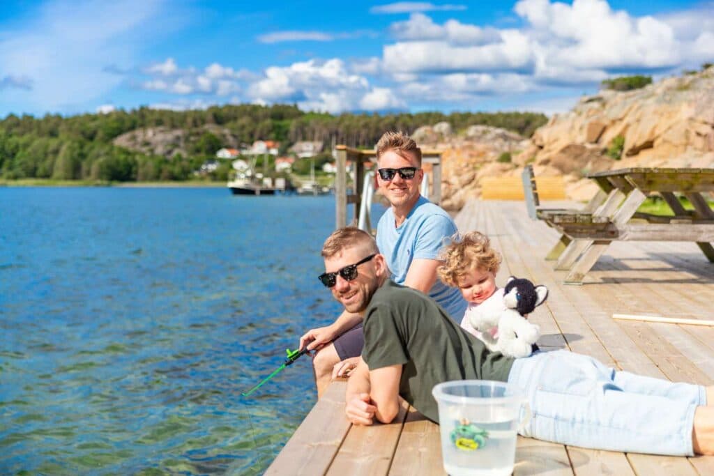 Familj med hund sitter på en brygga vid havet nära First Camp Edsvik – Grebbestad.