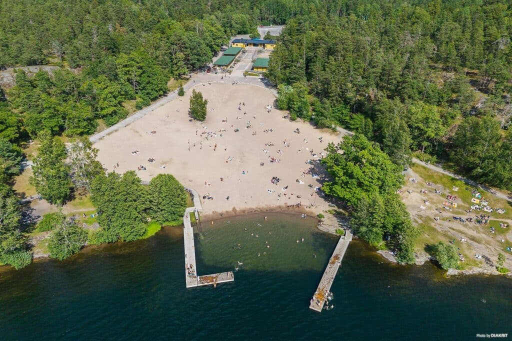 City Stockholm drönarbild över stranden med bryggor, människor som badar samt naturen.