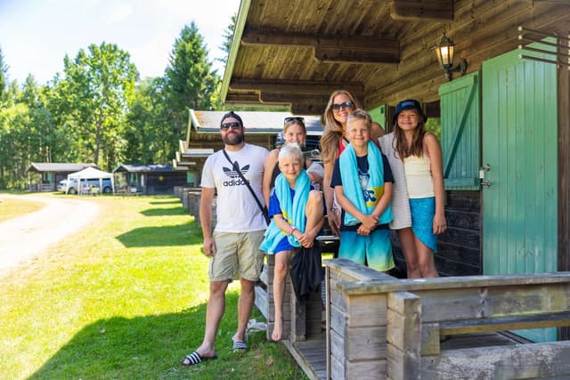 Familj som står med badhanddukar runt halsen utanför stugan på Skara Sommarland camping